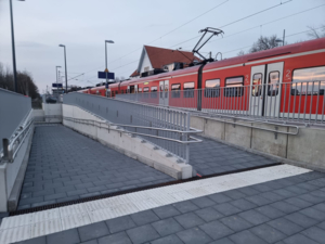 Rampe an einen Bahnhof mit einer S-Bahn im Hintergrund